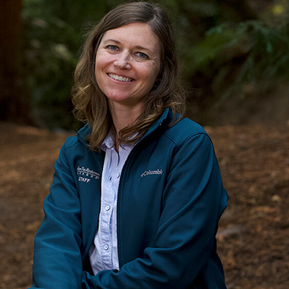 A woman wearing a dark teal jacket, sitting in a coast redwood forest