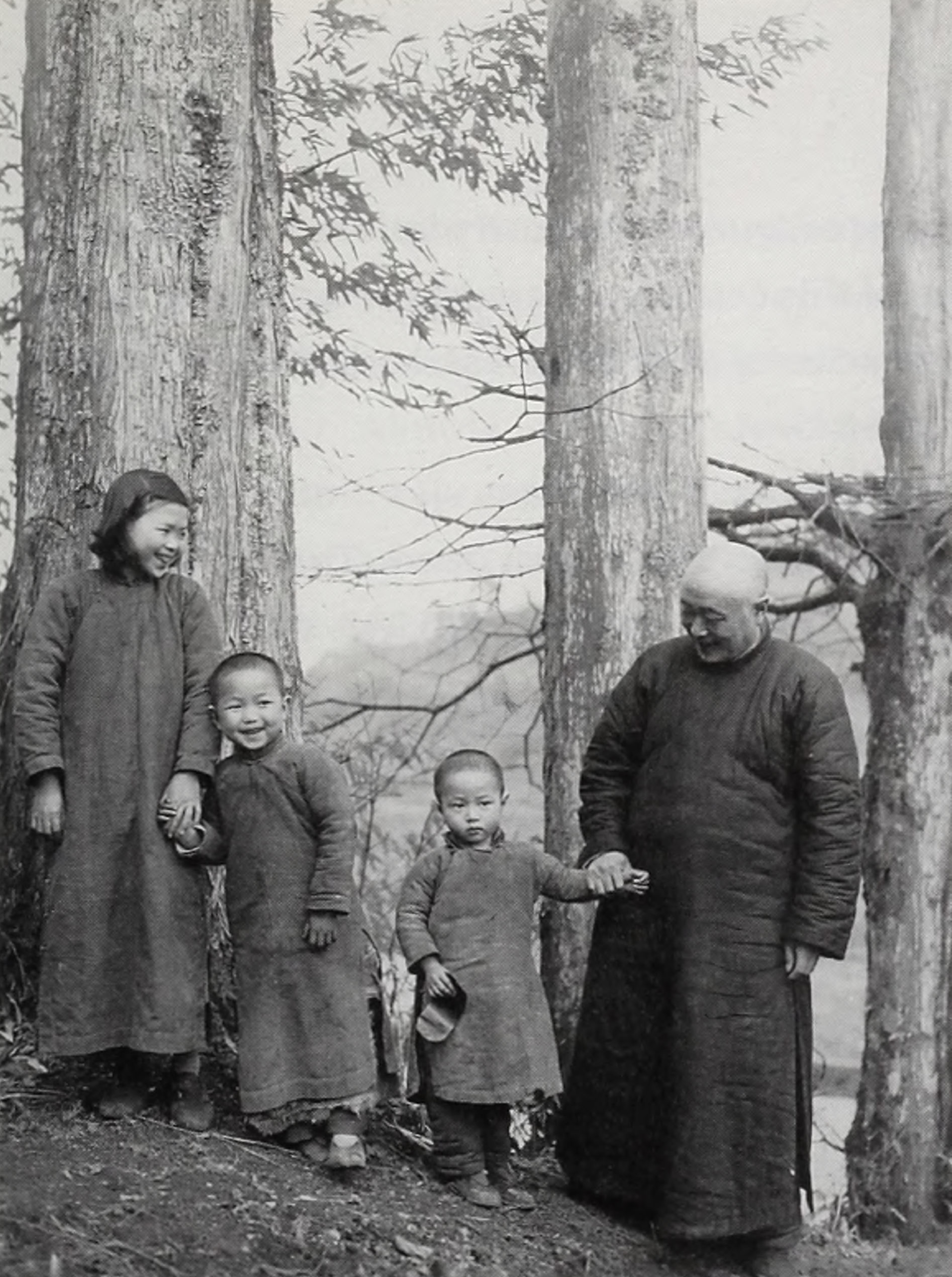 black and white photo of a family dressed in traditional Chinese tunics posing in front of three trees