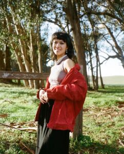 Emily Harwitz, a young woman of color with dark brown hair wearing a red jacket outdoors