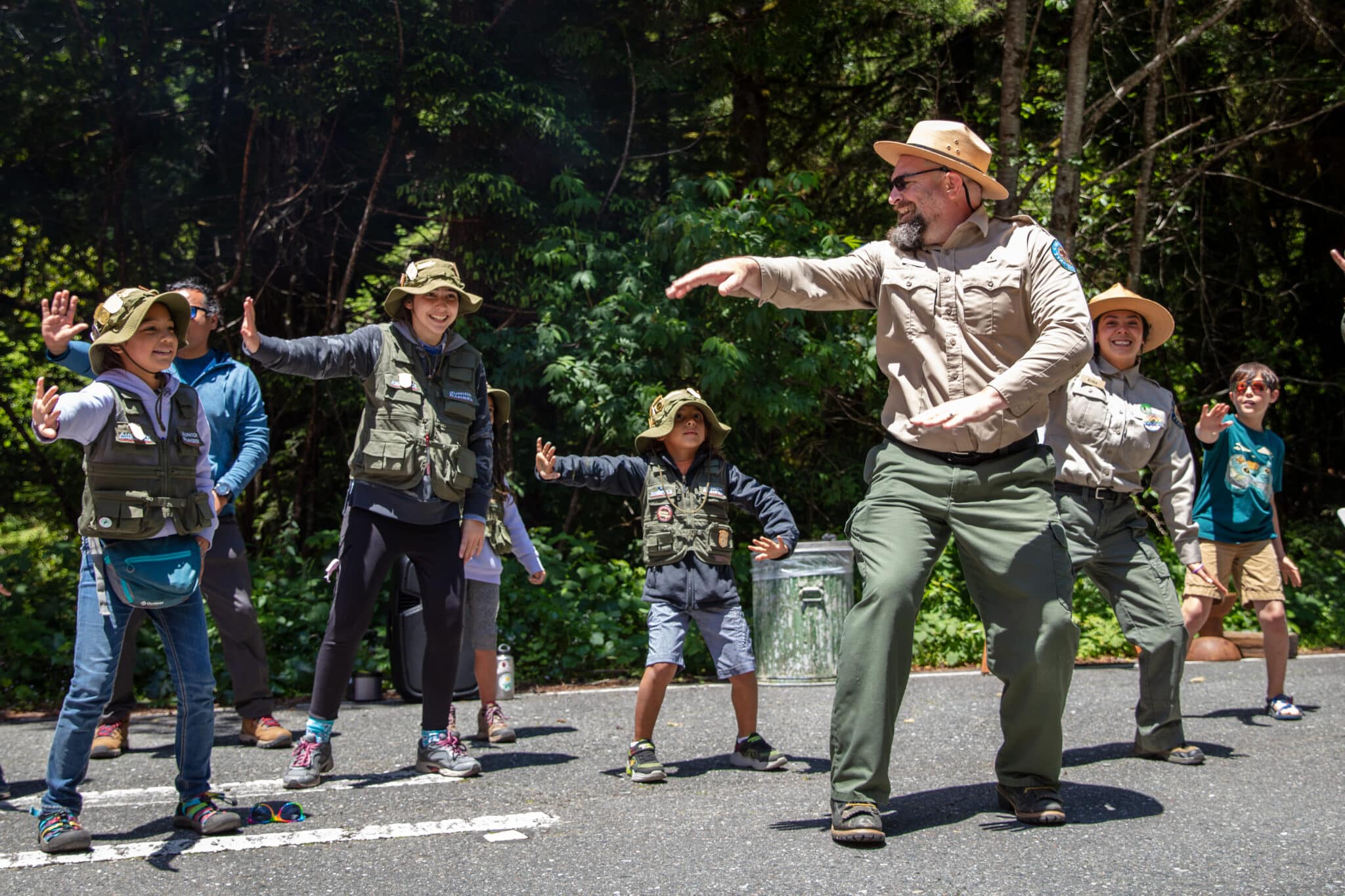 A man in a state parks uniform leads a group of young people in a dance