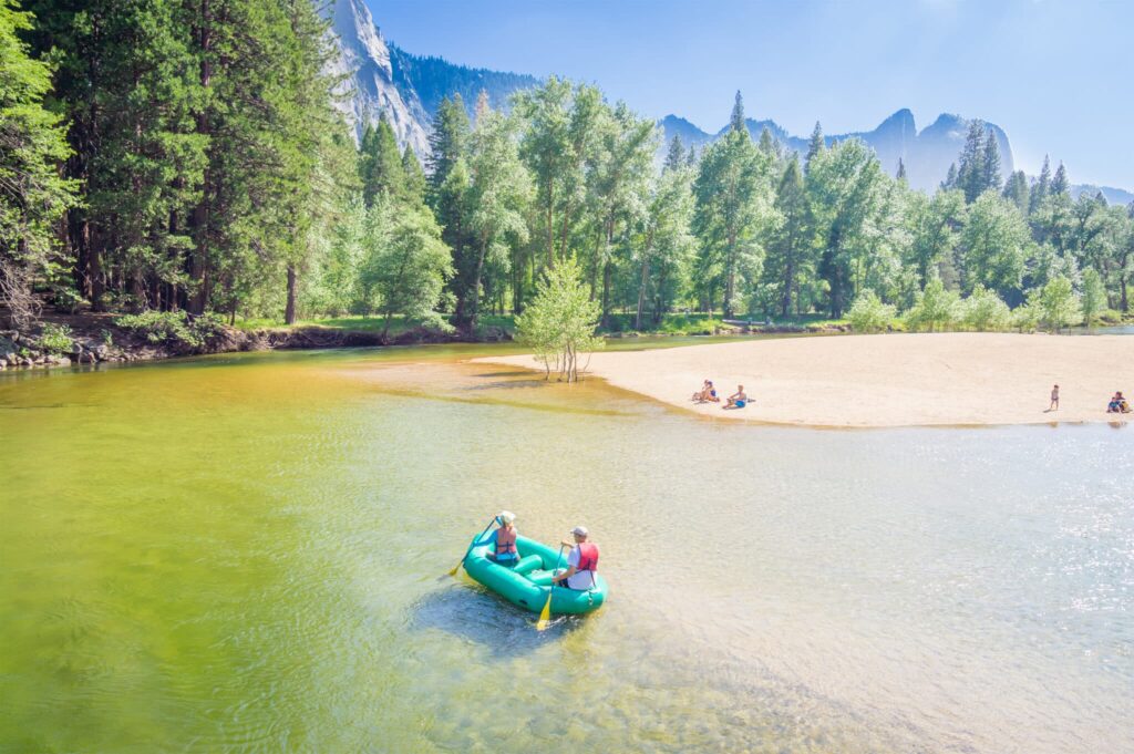 Two people in a bright blue inflatable raft on a shallow river near a beach