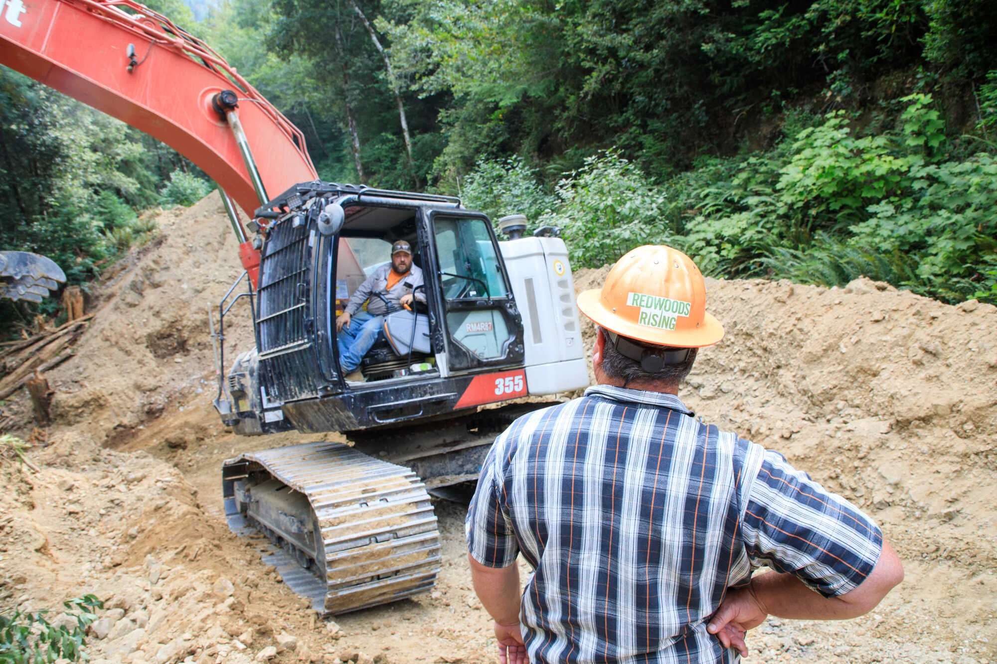 Two men in workwear speaking across a heavy machinery work site.