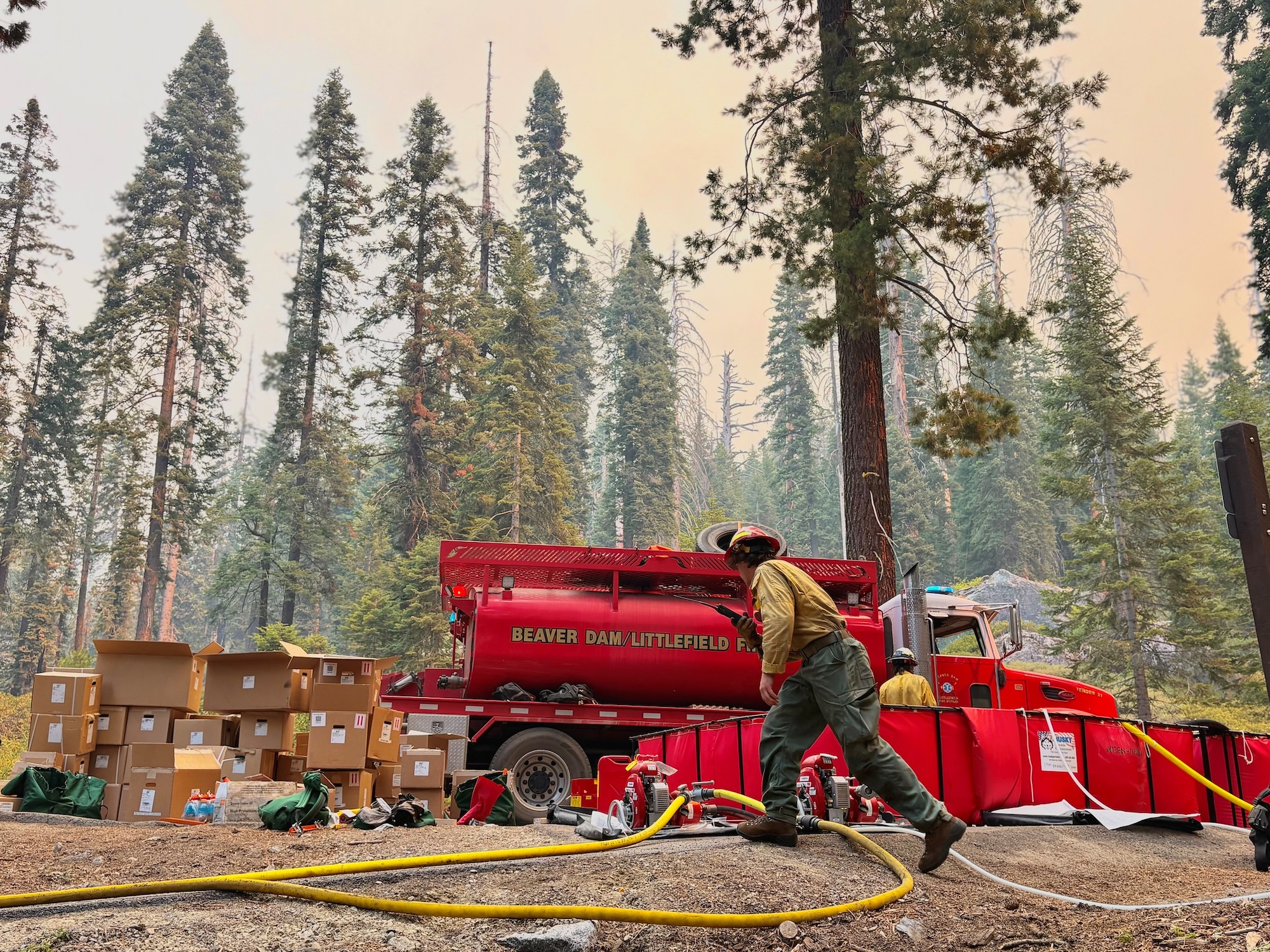 Fire fighter walks in front of water tanker during forest fire.