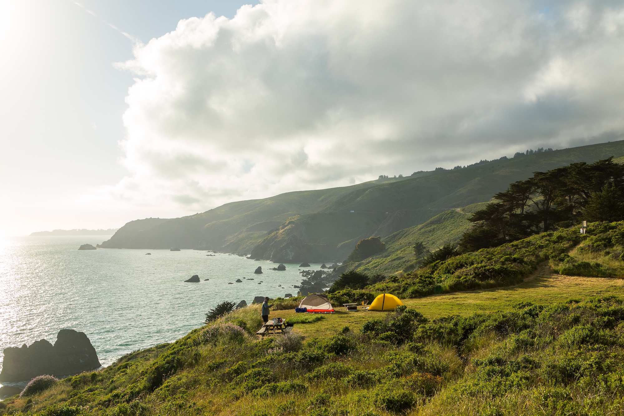 A green coastline with the water on the left side, and a yellow tent along the coast.
