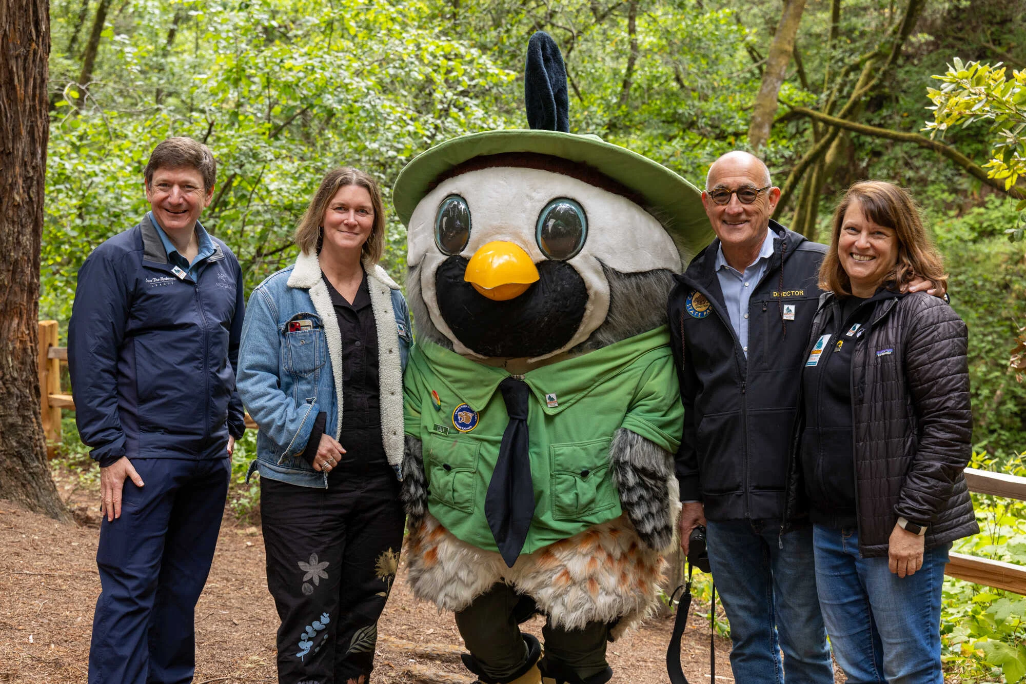 4 adults pose outdoors with California State Parks Week mascot.