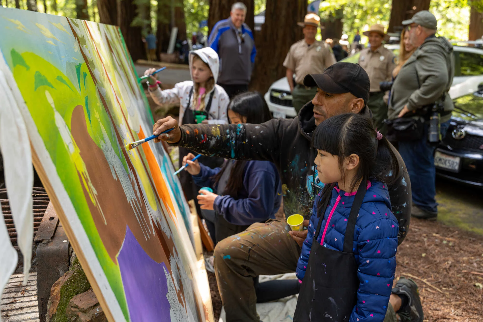 Man painting mural outdoors with other participants