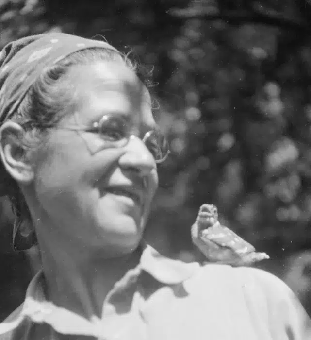 a black and white photo of a woman wearing glasses and a bandana with a bird on her shoulder