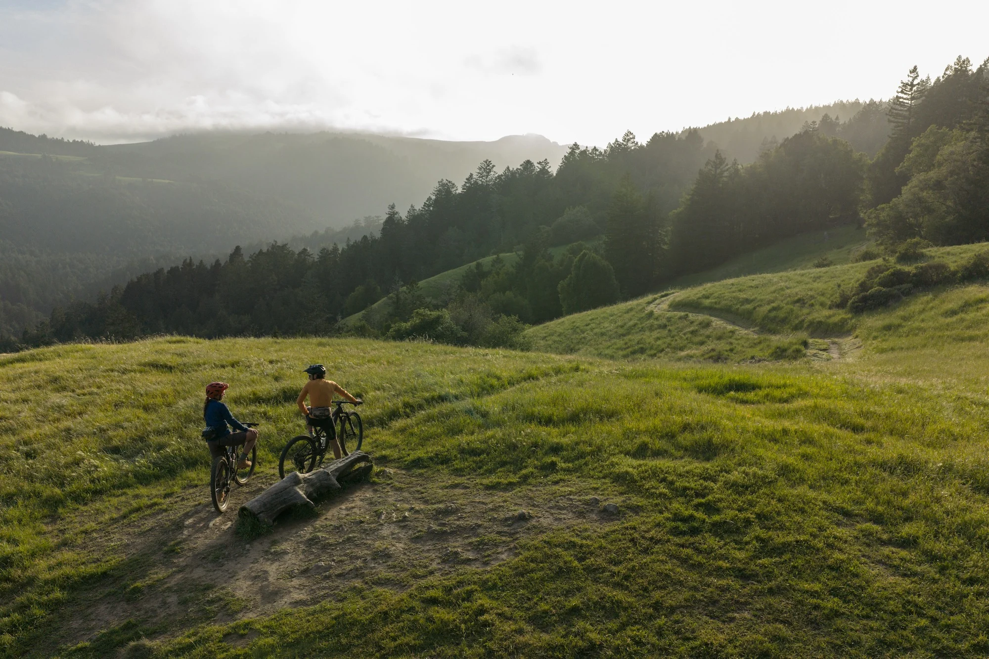 two bikers stand on a grassy hill