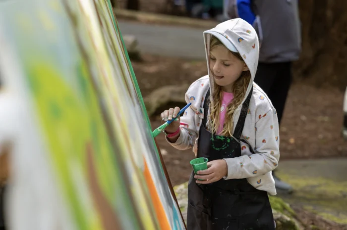 a young girl apples a paint bursh with green paint to a large canvas