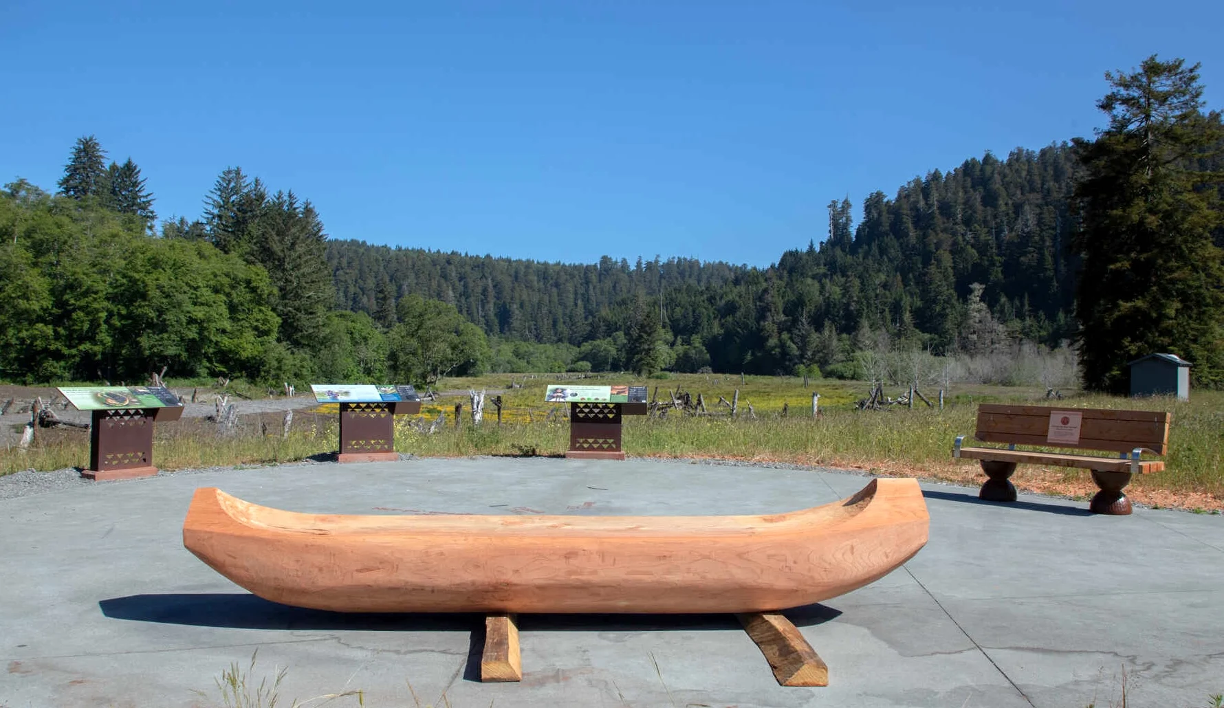 on the edge of a meadow, a canoe-shaped bench rests in front of interpretive displays