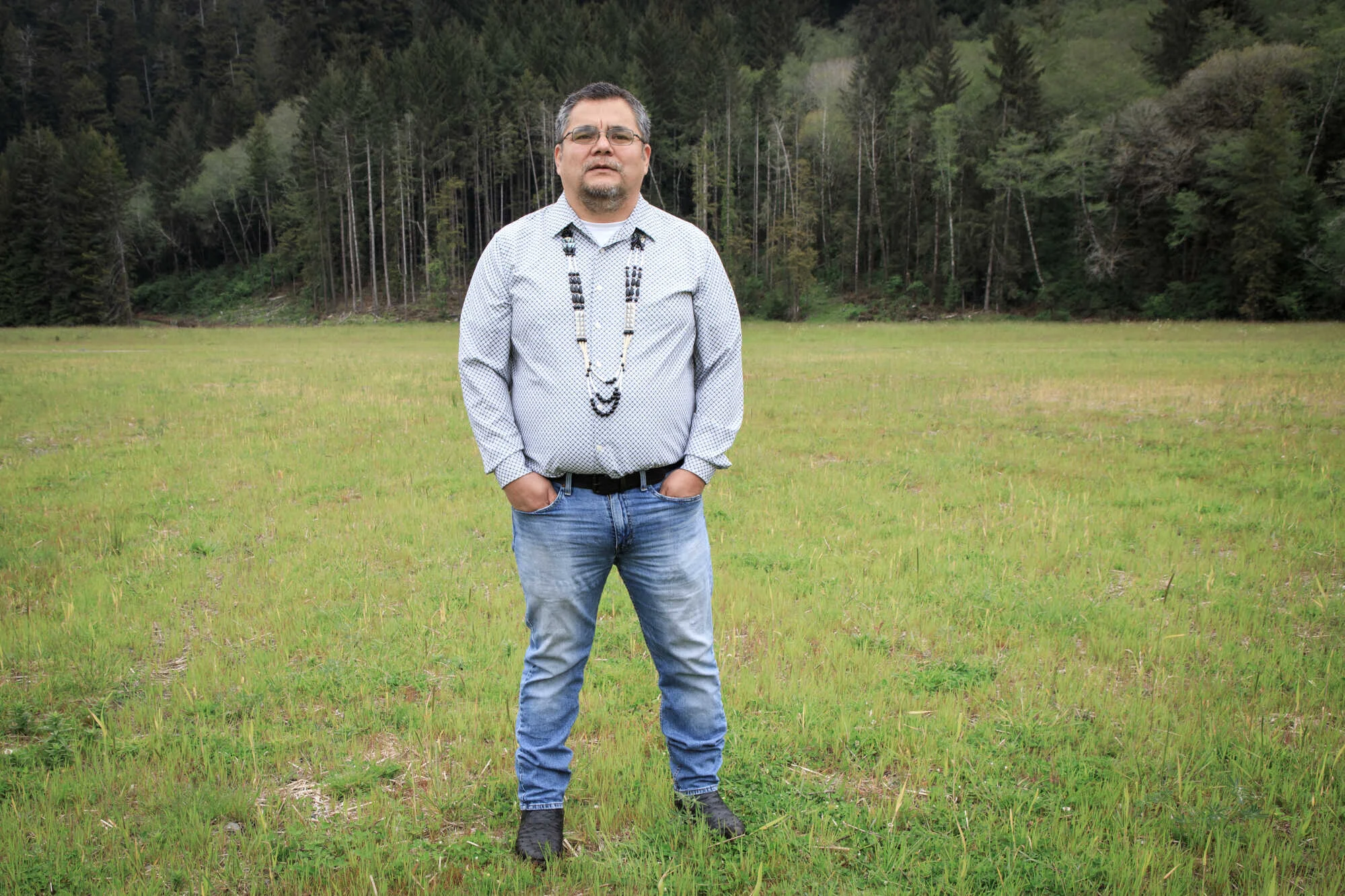 A Yurok tribal leader stands in an open meadow and gazes at the camera