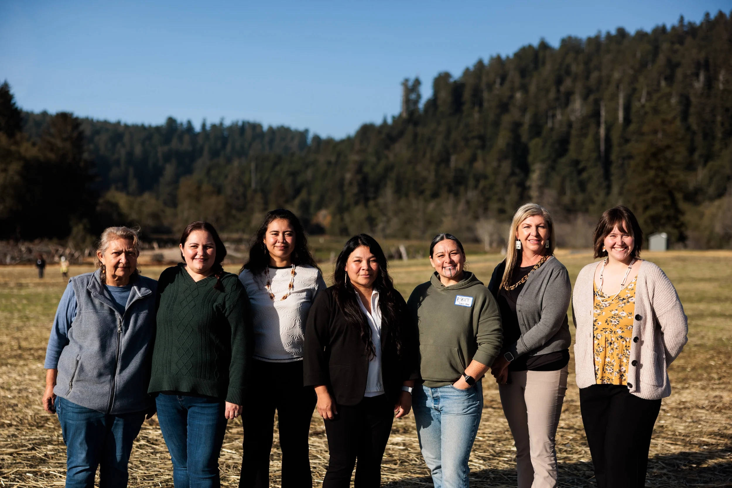 a group of women pose proudly in front of a meadow backed by redwoods