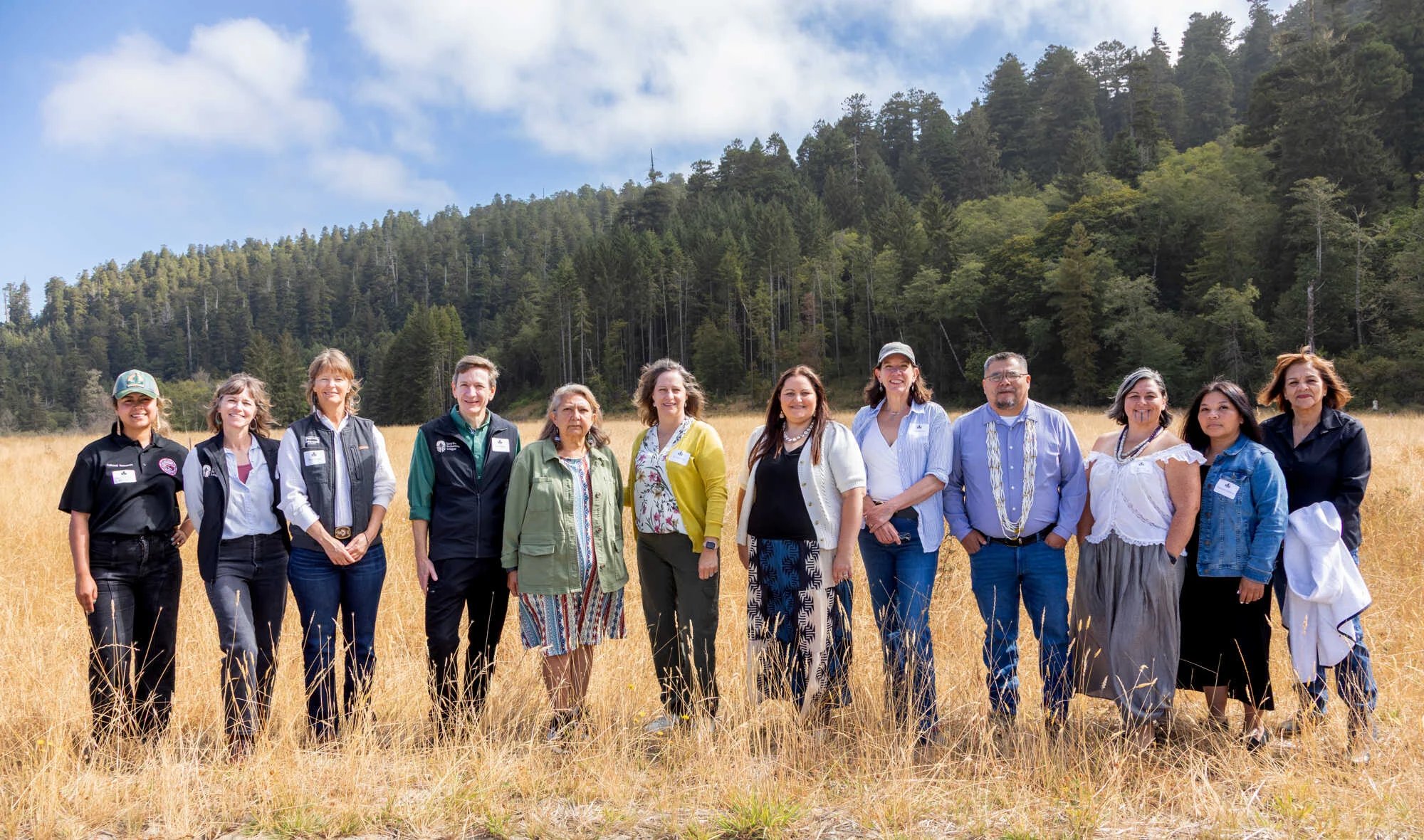12 representatives of the collective partnership stand in the field for a group photo.