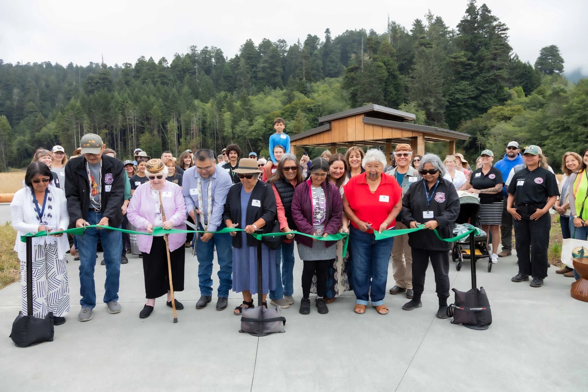 A group of Yurok Tribal members cutting a green ribbon ribbon in front of the new gateway on opening day.