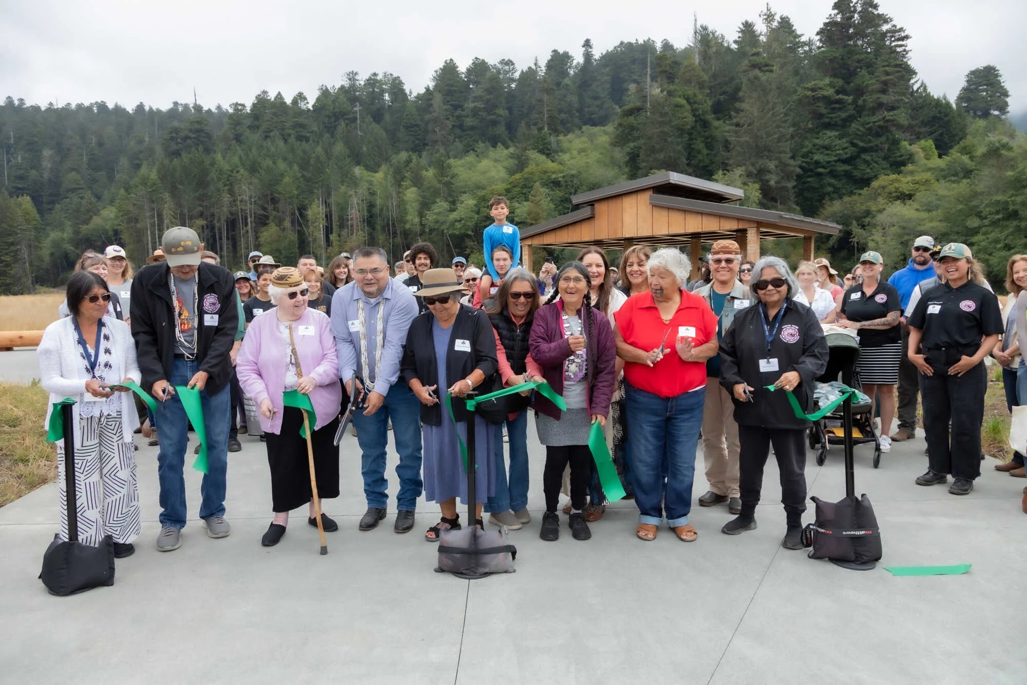 A group of Yurok Tribal members cutting a green ribbon ribbon in front of the new gateway on opening day.