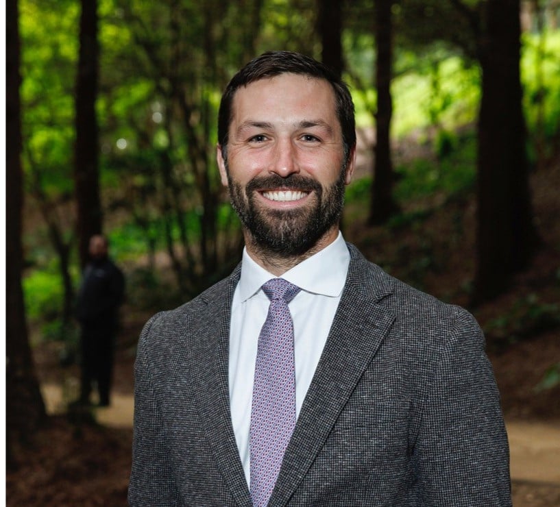 Person smiling in suit and tie in shaded forest